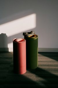 Two rolled yoga mats standing against a wall in soft morning light.