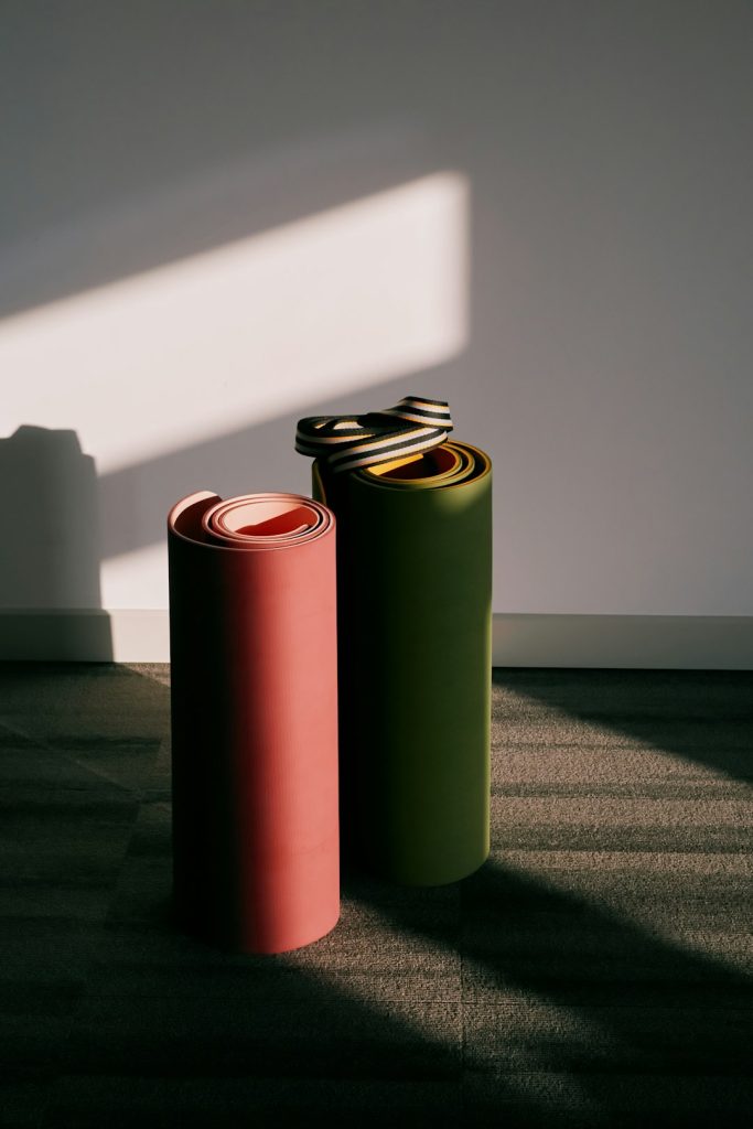 Two rolled yoga mats standing against a wall in soft morning light.