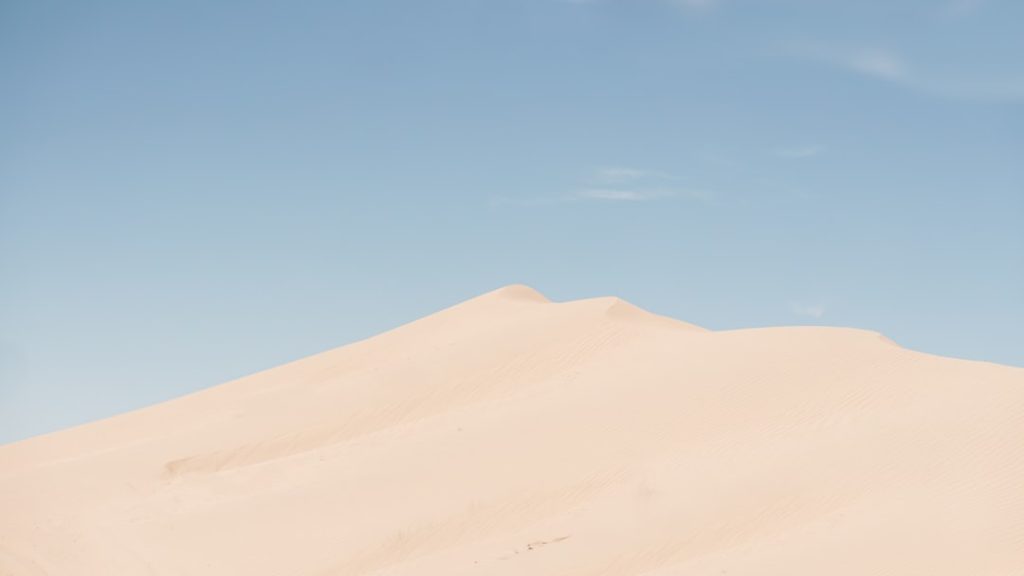 Soft desert dunes under warm light and open sky.