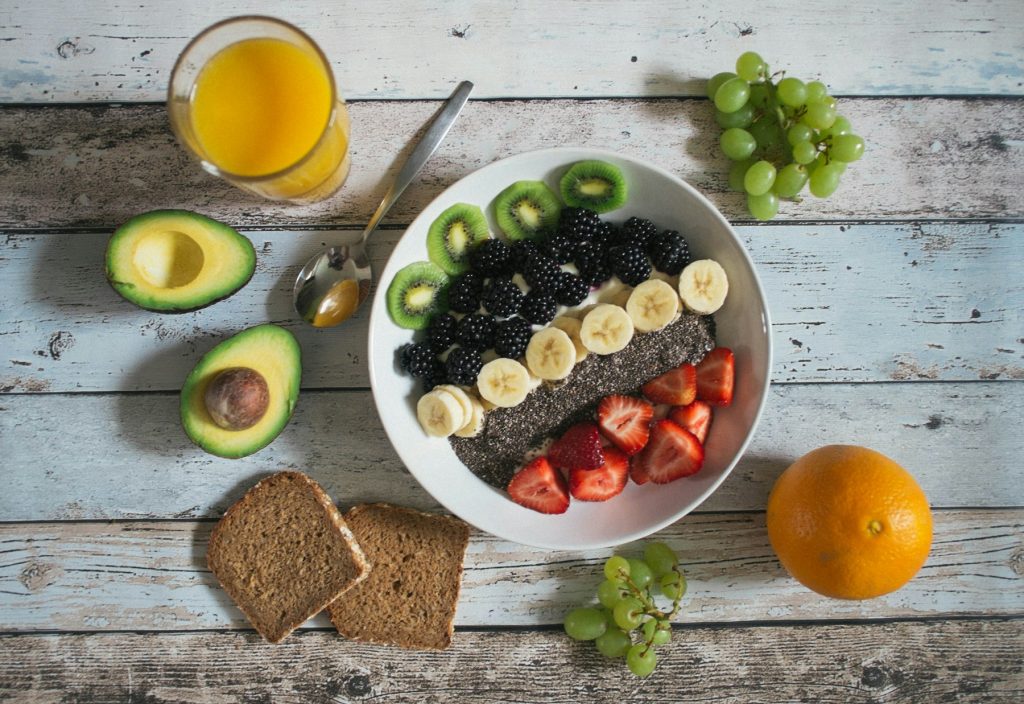 A spread of fresh whole foods including fruit, avocado, orange juice and wholegrain bread.