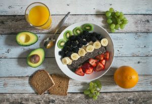A spread of fresh whole foods including fruit, avocado, orange juice and wholegrain bread.