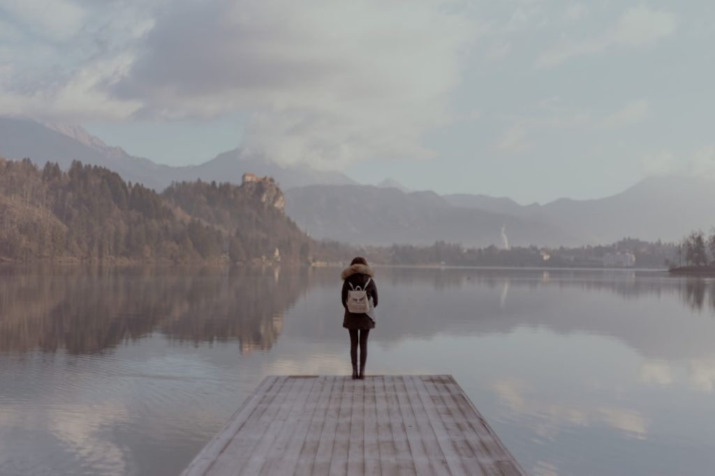 A lone figure standing beside still water in a quiet landscape.