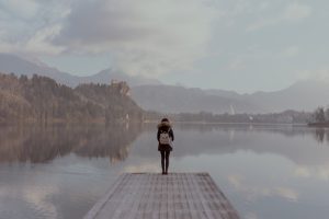 A lone figure standing beside still water in a quiet landscape.